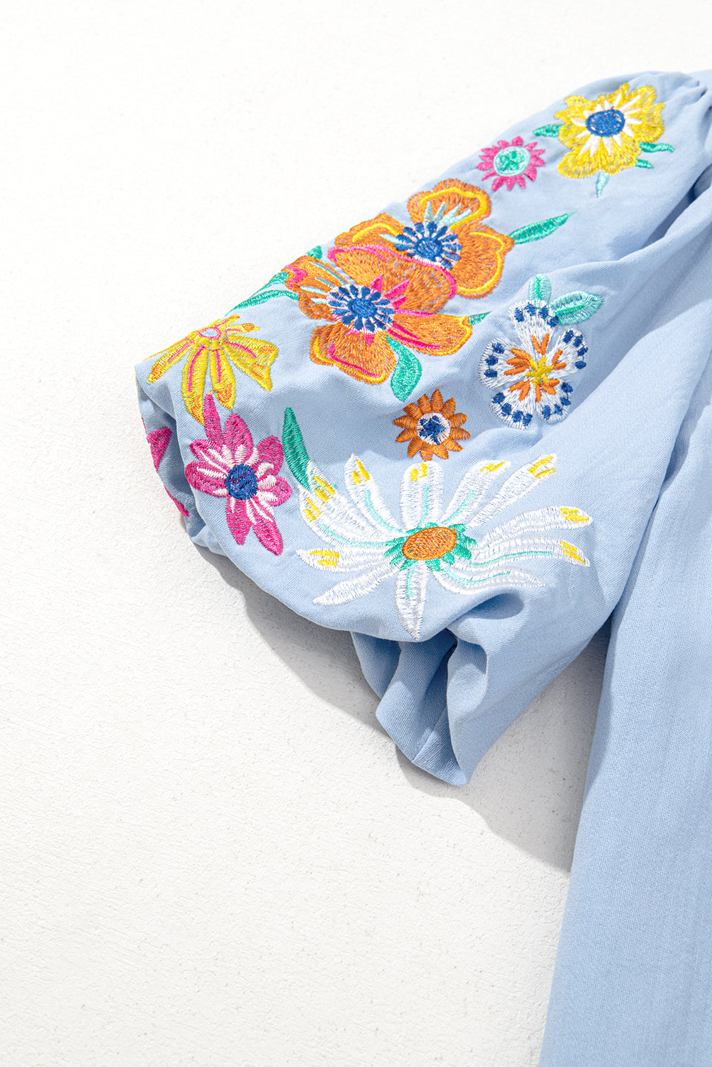 Light blue fabric with colorful floral embroidery on a white background