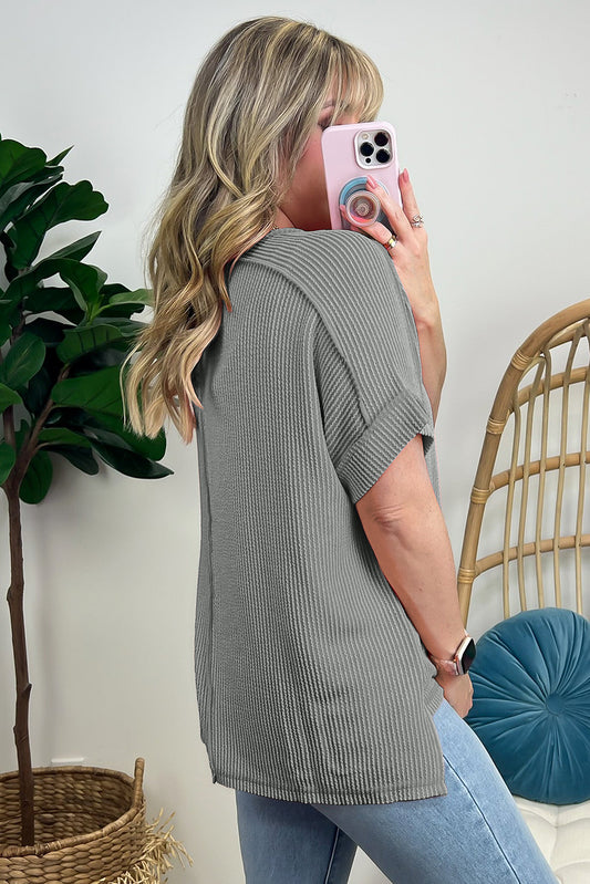 Woman taking a mirror selfie wearing a gray ribbed sweater and blue jeans, with a plant and chair in the background.