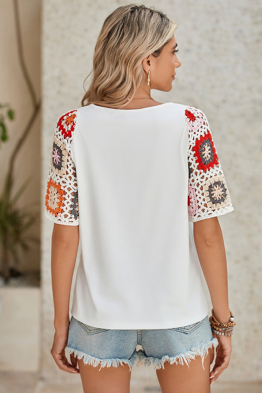 Woman wearing a white top with colorful crochet sleeves against a neutral background