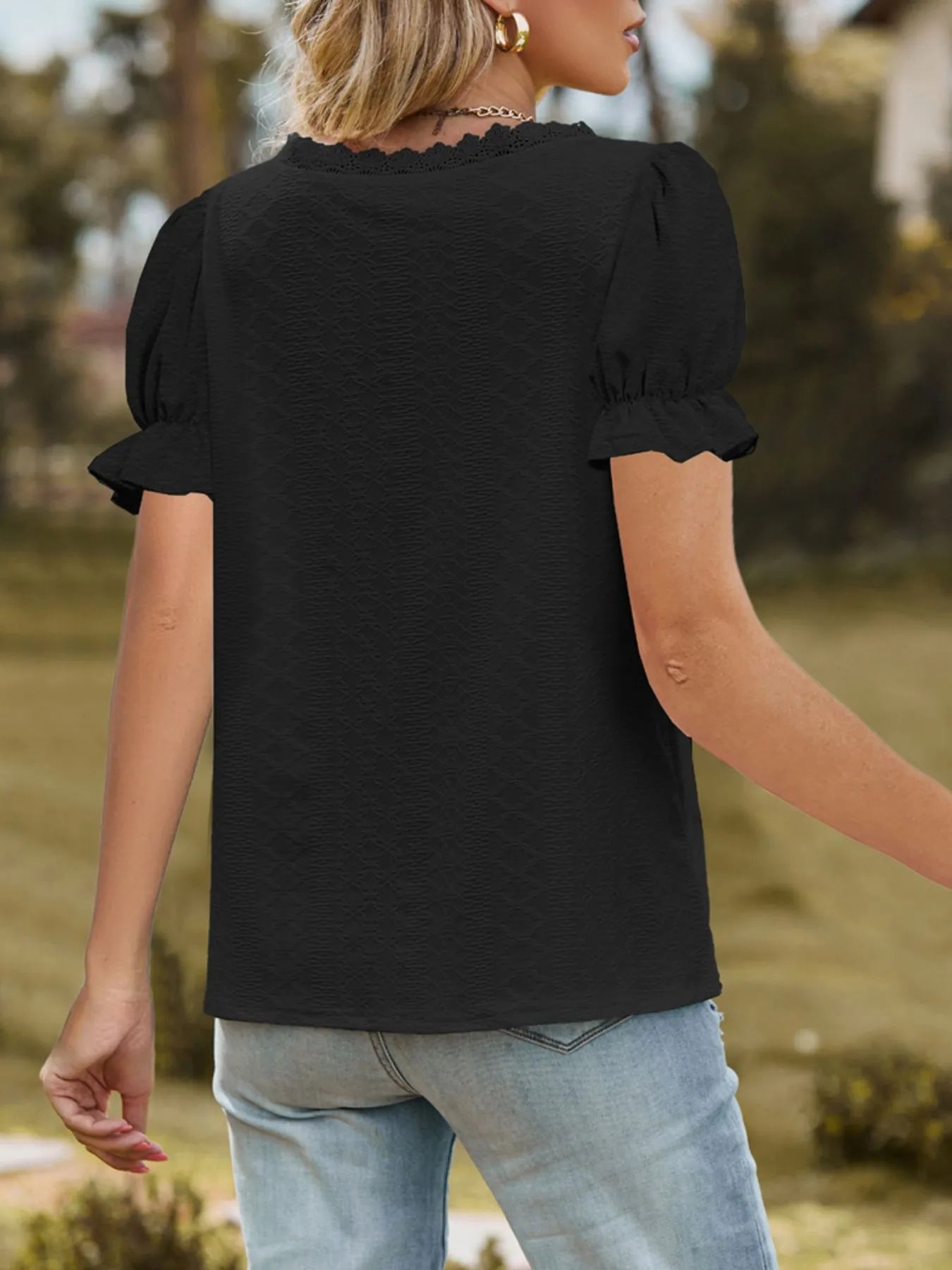 Person wearing a black top with ruffled sleeves and light blue jeans outdoors.