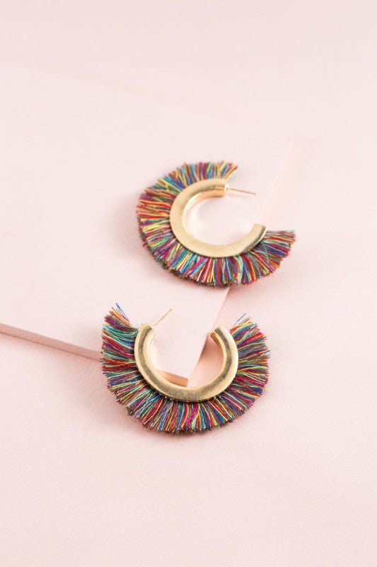 Colorful fringe earrings on a pink background