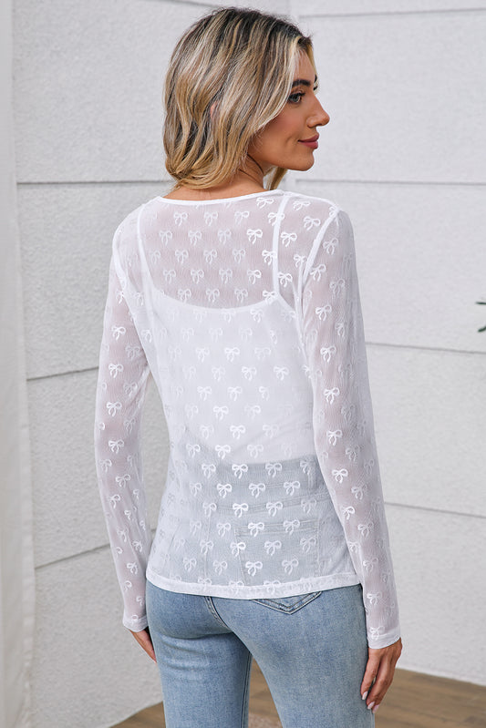 Woman wearing a white lace long-sleeve top and light blue jeans against a neutral background