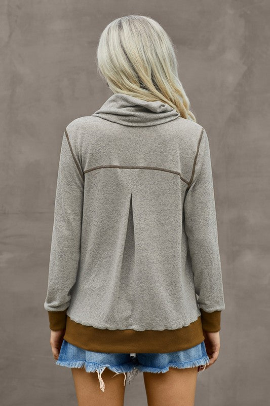 Person wearing a gray zip-up hoodie with brown trim against a plain background