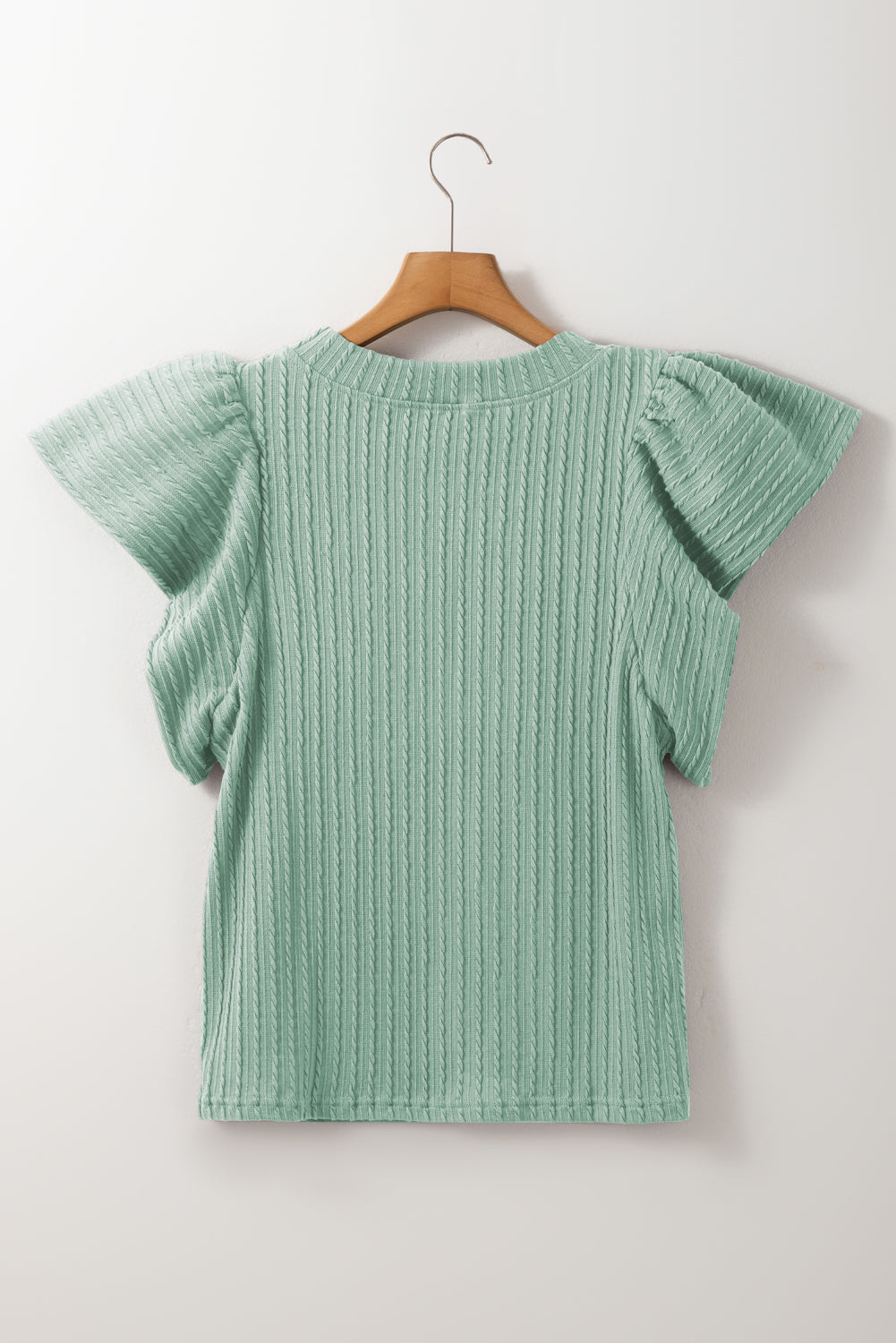 Green ribbed sweater with ruffled sleeves on a wooden hanger against a white background