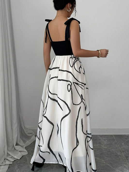 Woman wearing a black top and white dress with black abstract patterns, standing against a gray curtain.
