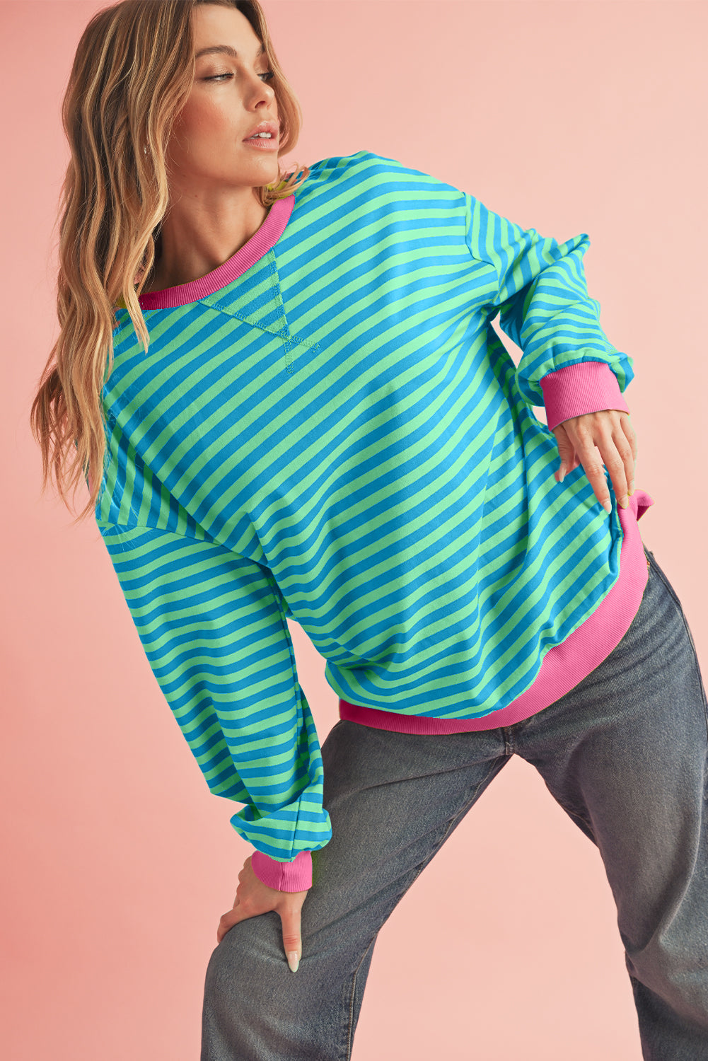 Woman wearing a blue and pink striped sweater with a pink shirt underneath on a pink background