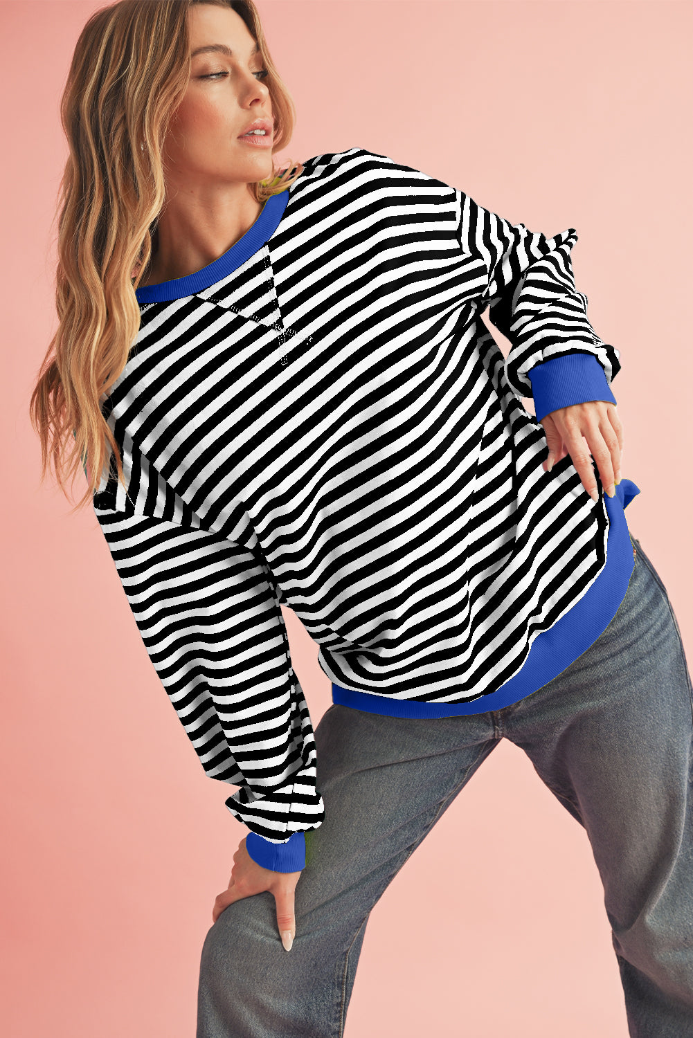 Woman wearing a black and white striped sweater with blue trim on a pink background