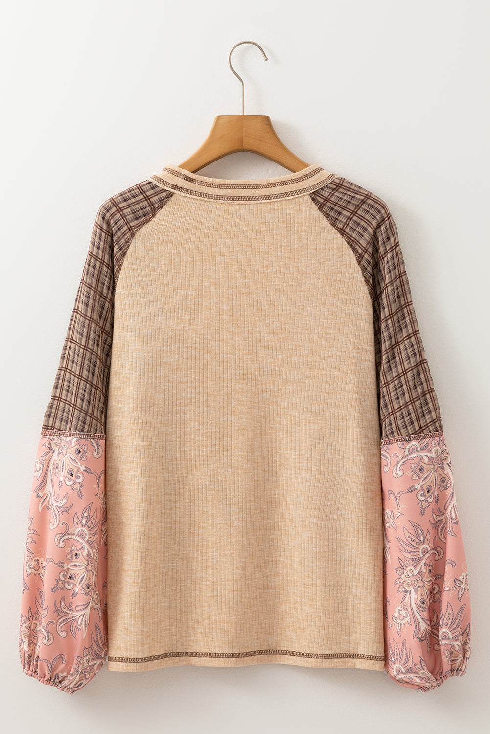 Beige sweater with plaid and floral sleeves on a wooden hanger against a white background