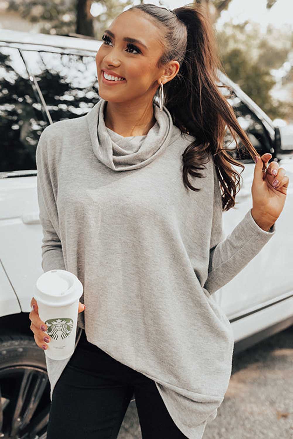 Woman in a gray sweater holding a Starbucks cup outdoors.