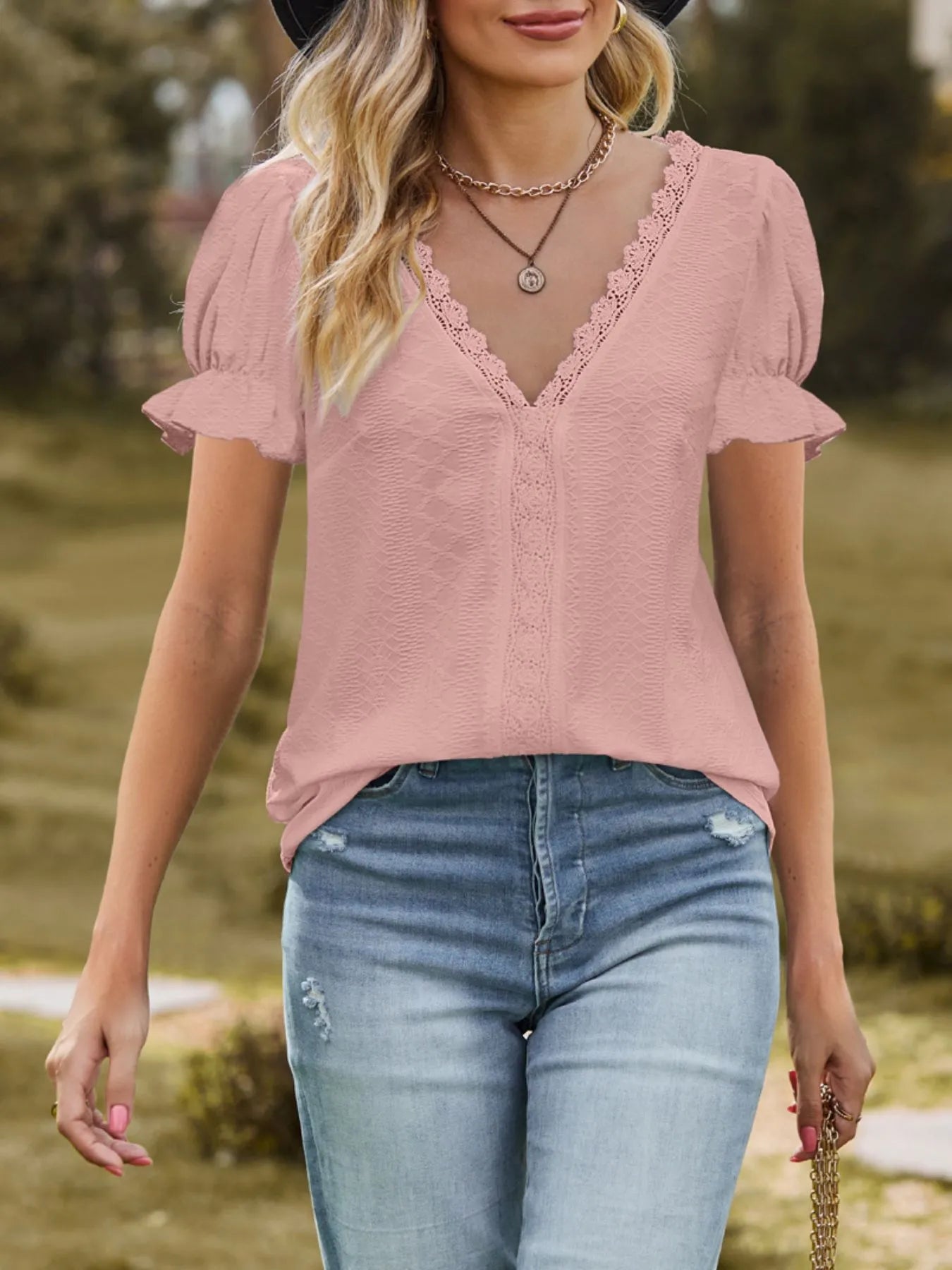 Woman wearing a pink blouse with lace details and blue jeans outdoors.