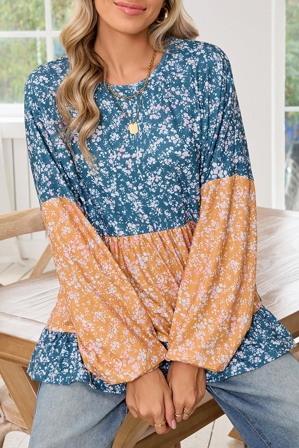 Woman wearing a floral two-tone top sitting on a wooden chair.