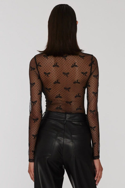 Person wearing a black fishnet top with bow patterns and black leather pants on a white background