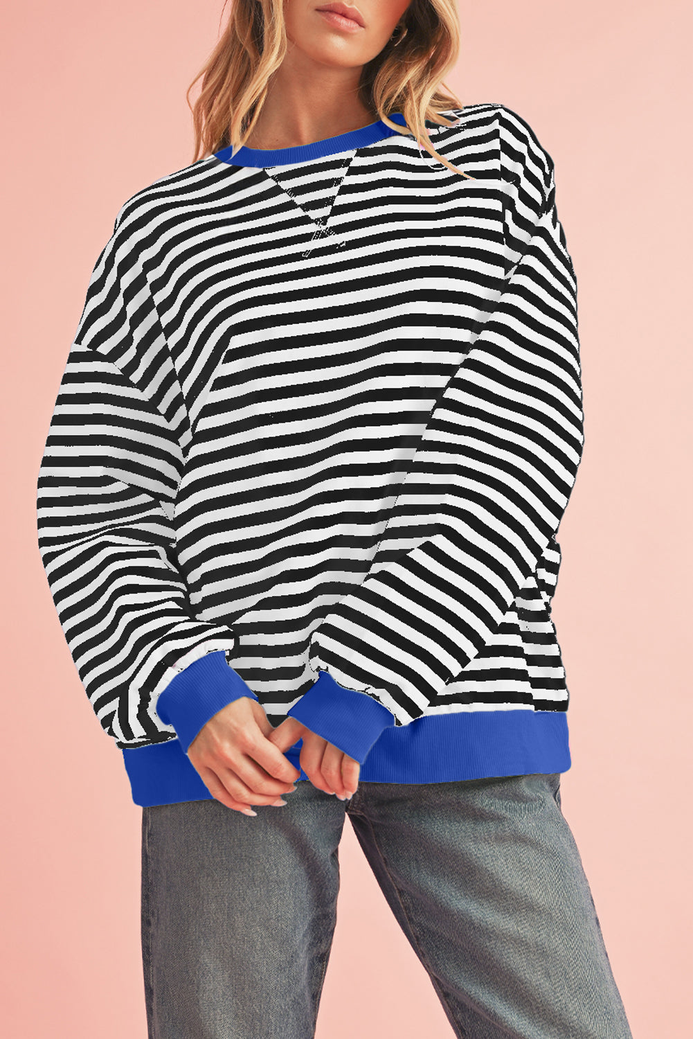Person wearing a black and white striped sweater with blue trim on a pink background