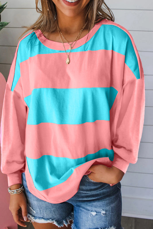 Person wearing a pink and blue striped sweater with denim shorts against a light wooden panel background.
