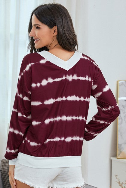 Woman wearing a maroon and white tie-dye sweater with a blurred indoor background