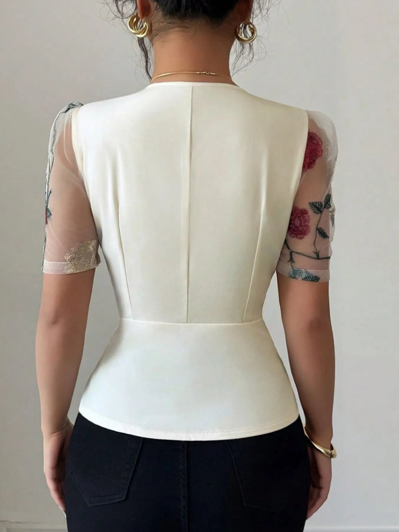 Person wearing a white top with sheer sleeves against a plain background