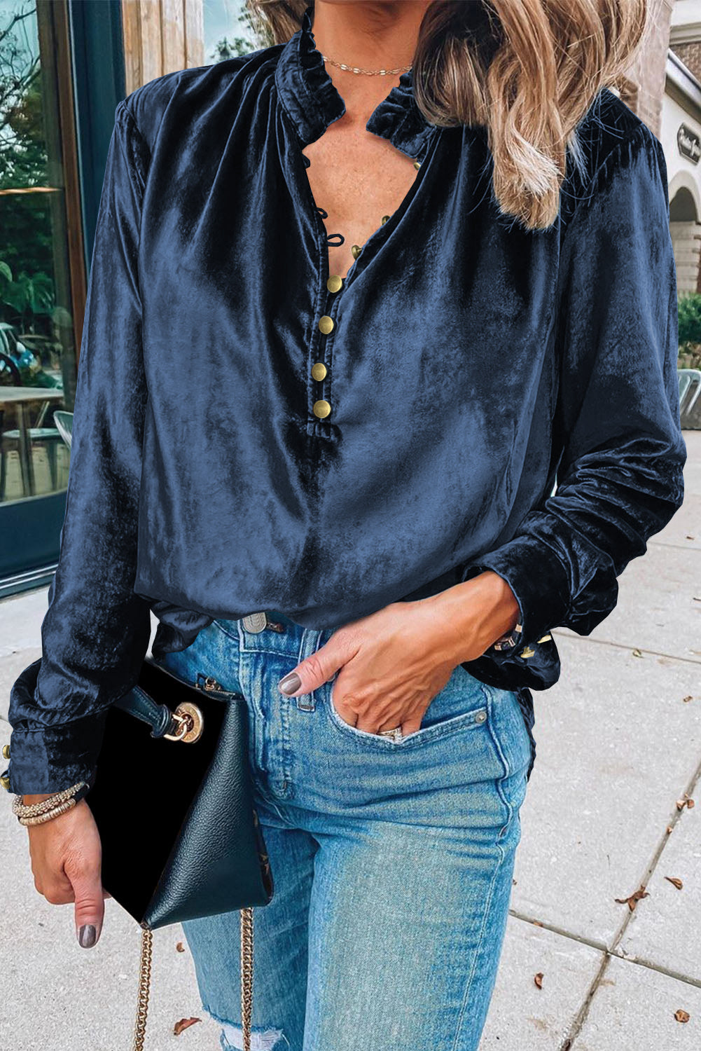 Person wearing a dark blue satin shirt and jeans, holding a black handbag.