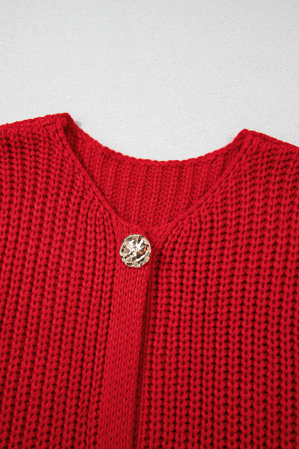 Close-up of a red knitted garment with a gold button on a light gray background