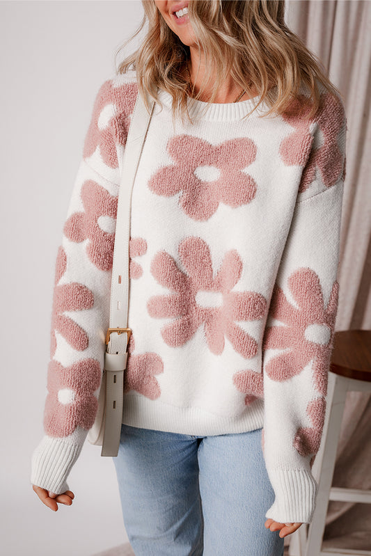 Person wearing a white sweater with pink floral patterns and light blue jeans.