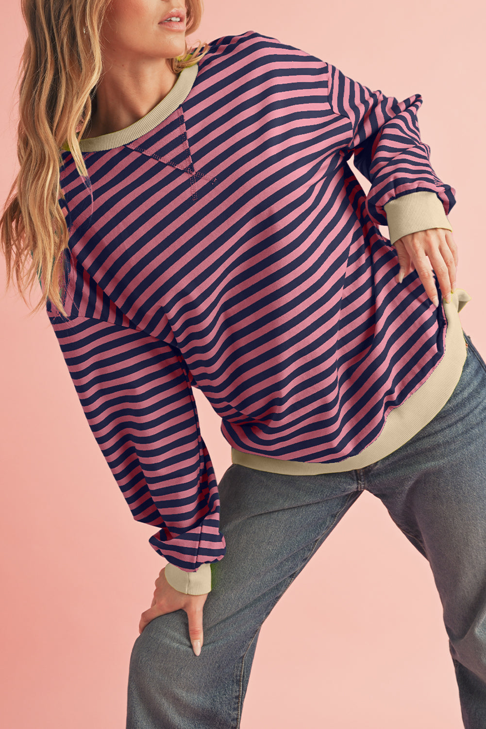 Person wearing a striped long-sleeve top and jeans on a pink background
