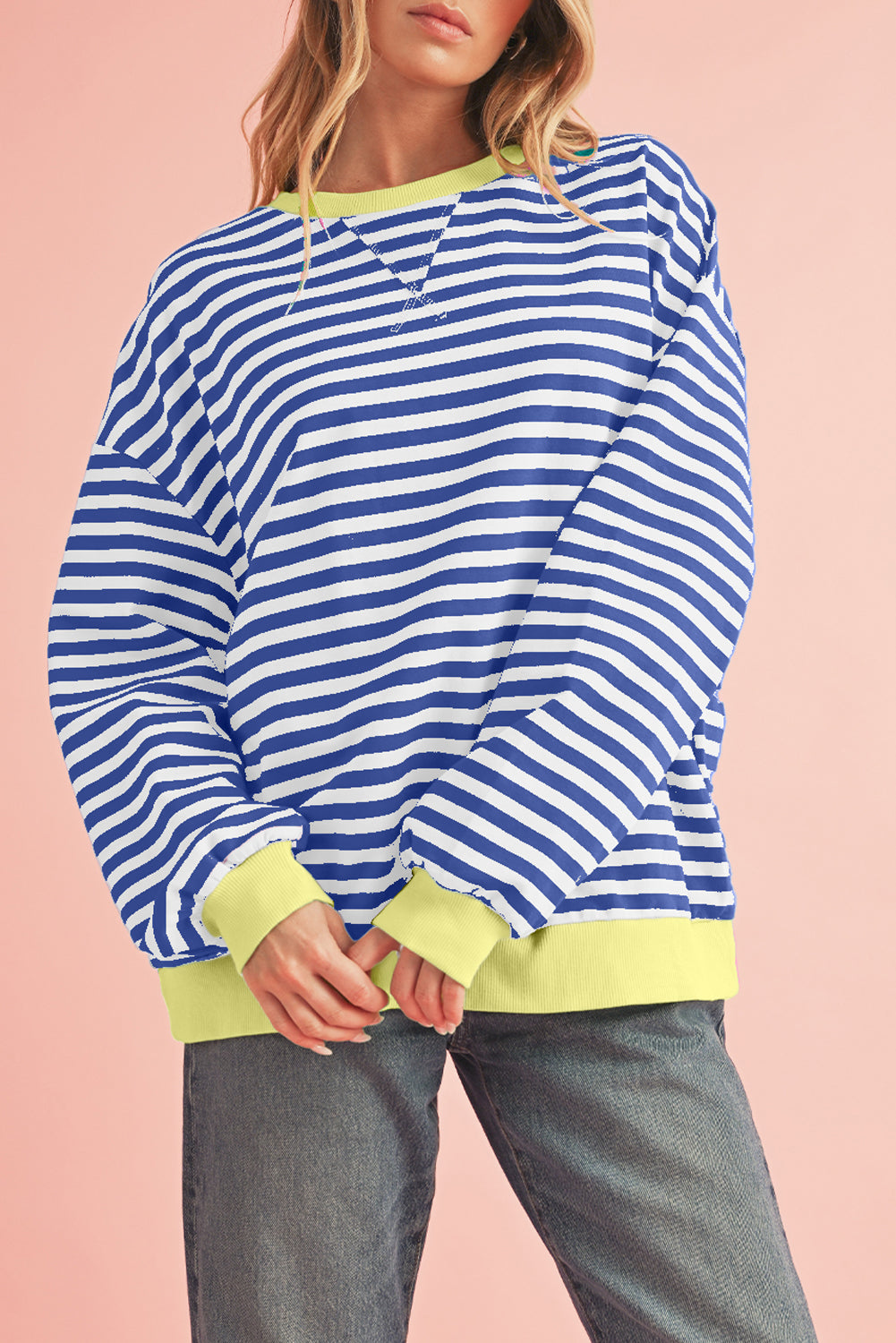 Person wearing a blue and white striped sweater with green accents on a pink background