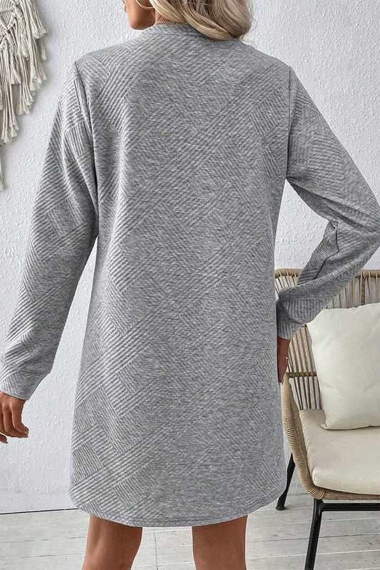 Person wearing a gray dress with long sleeves in an indoor setting.