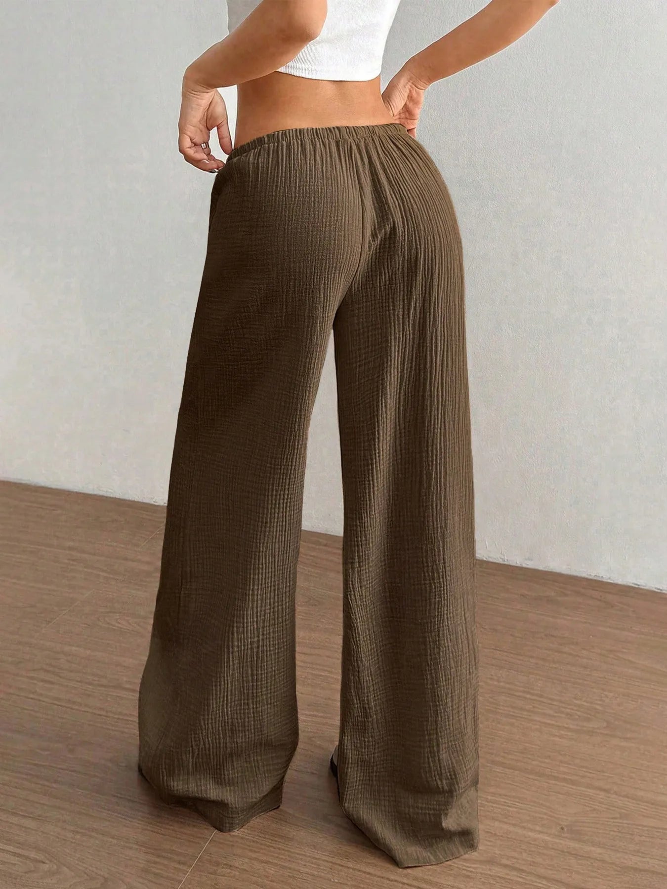 Brown wide-leg pants worn by a person on a wooden floor with a neutral background