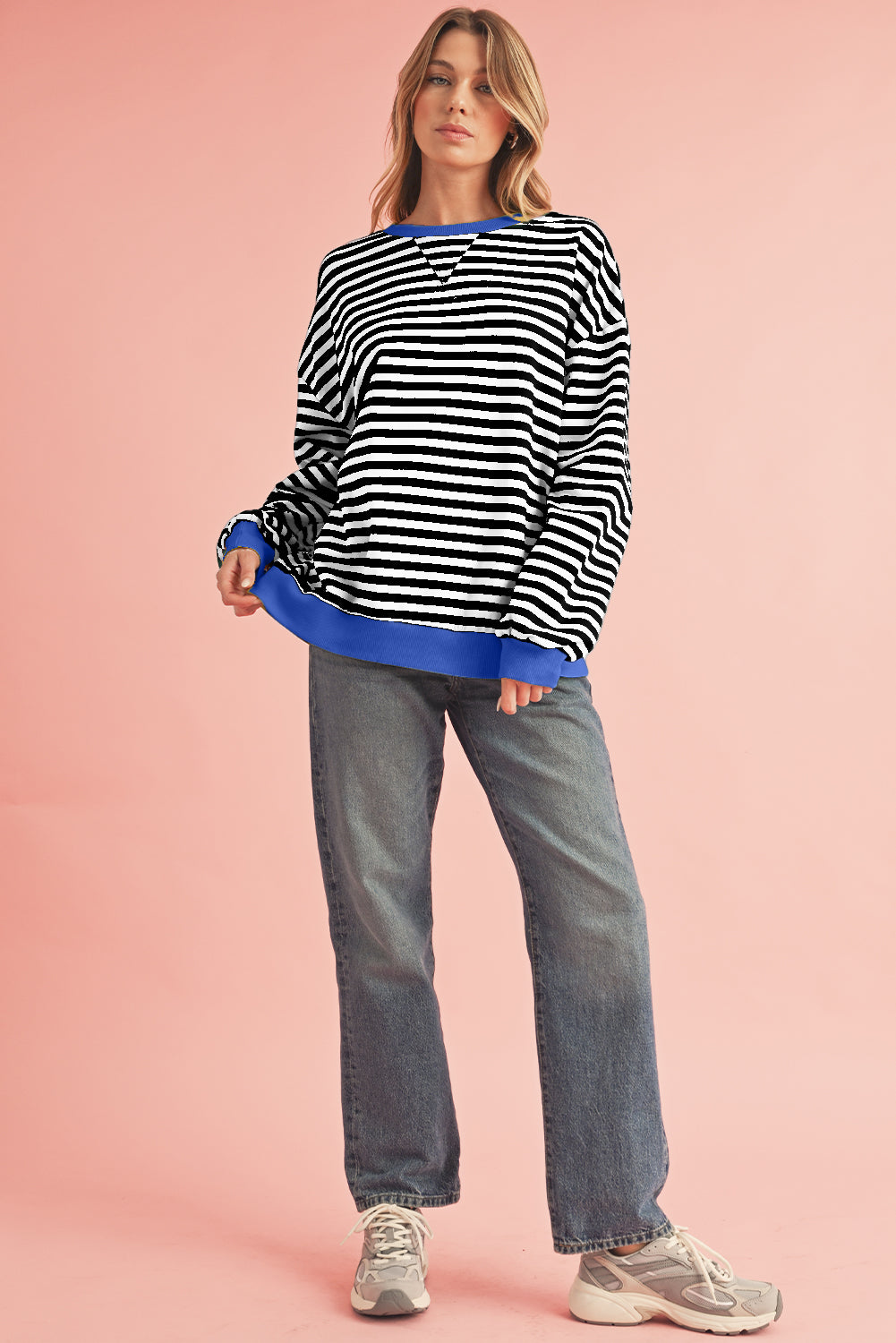 Woman wearing a black and white striped sweater with blue trim on a pink background