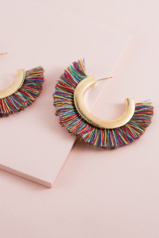 Colorful fringe earrings on a pink background