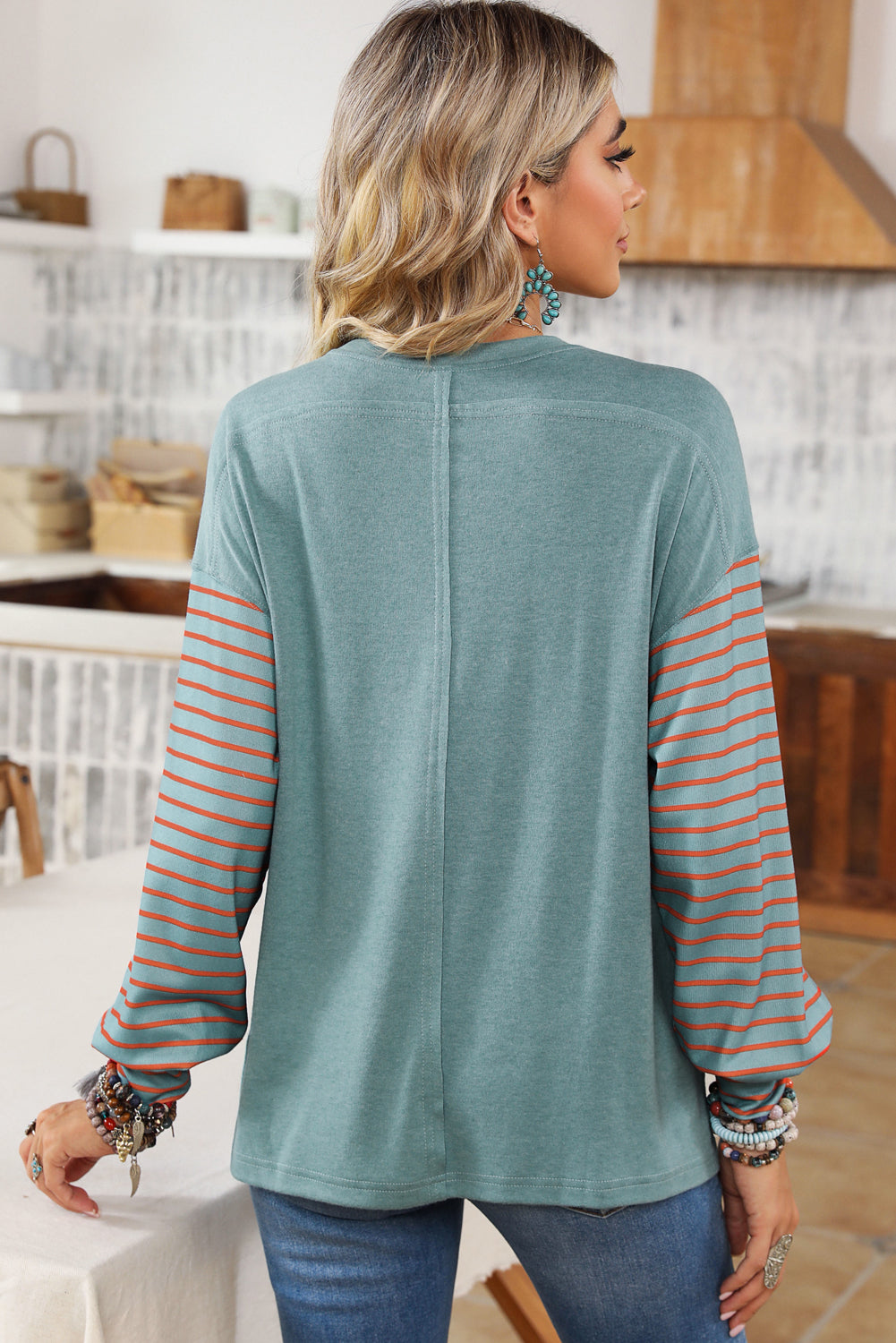 Woman wearing a teal sweater with striped sleeves in a kitchen setting