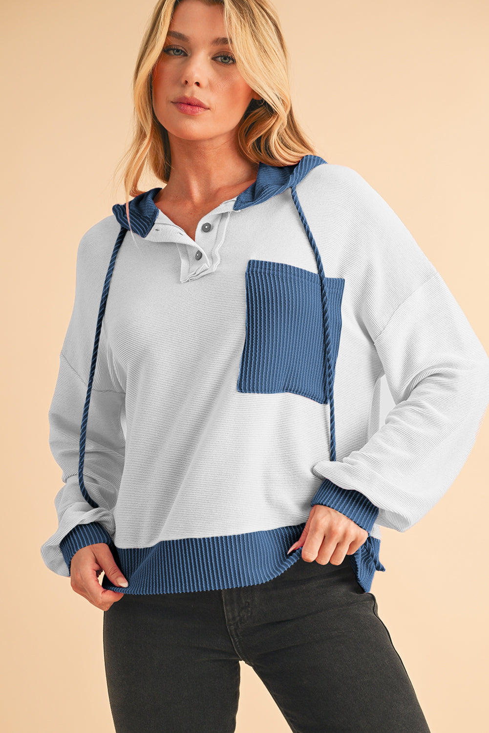 Woman wearing a light blue and navy color-blocked sweater on a beige background