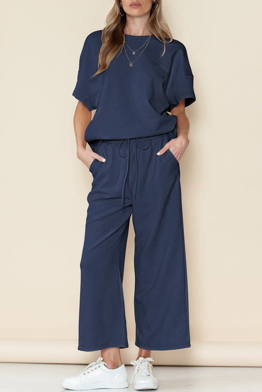 Person wearing a navy blue outfit with wide-leg pants and a matching top against a beige background