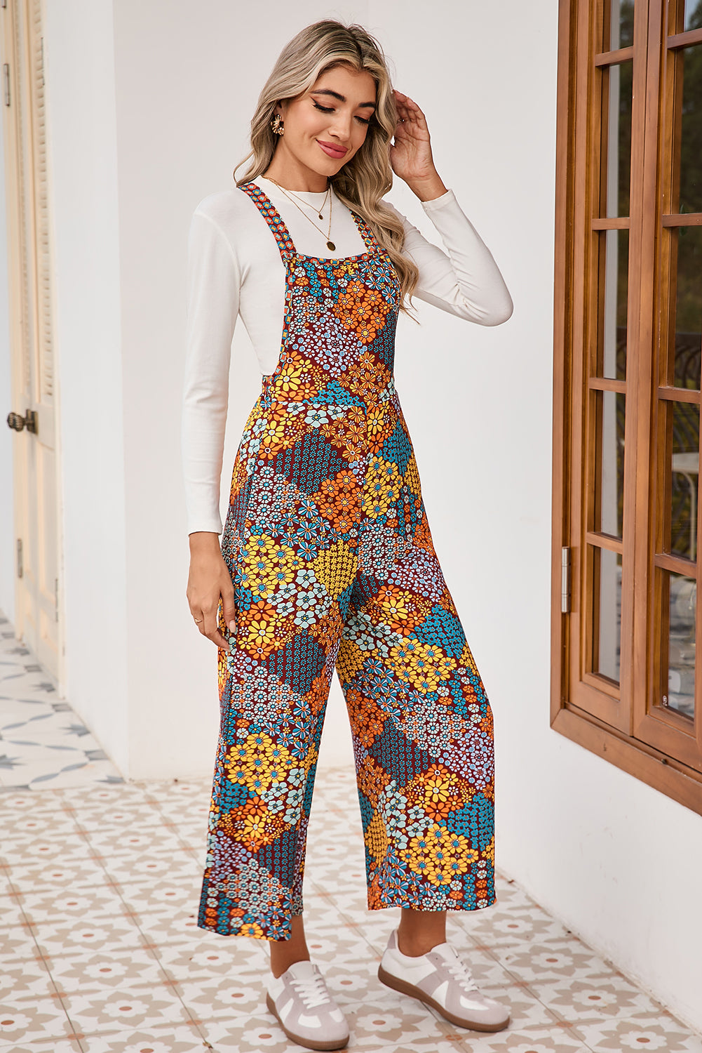 Woman wearing a colorful floral jumpsuit standing in a room with a wooden door.
