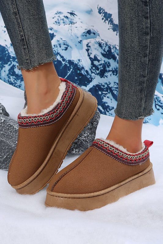 Brown slippers with patterned trim worn by a person in snow.