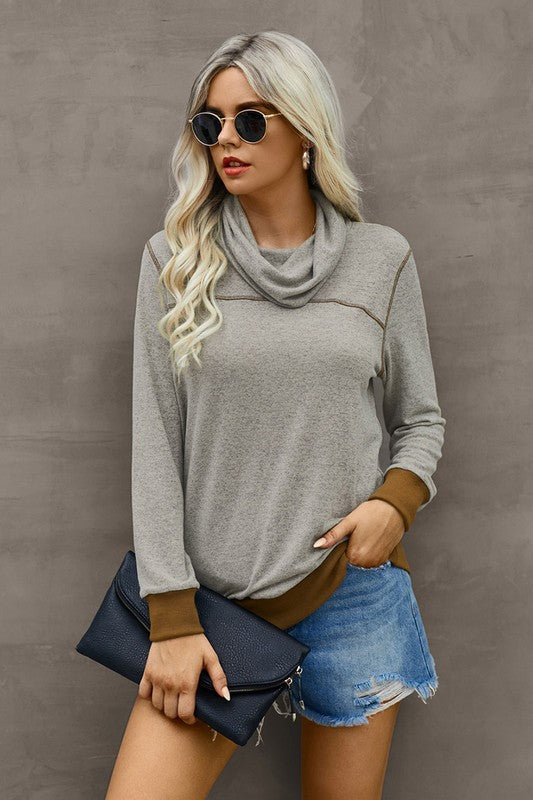 Woman wearing a gray sweater, denim shorts, and sunglasses against a plain background