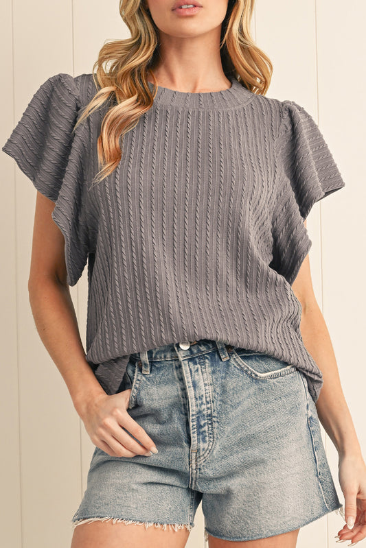 Woman wearing a gray ribbed top and denim shorts against a neutral background