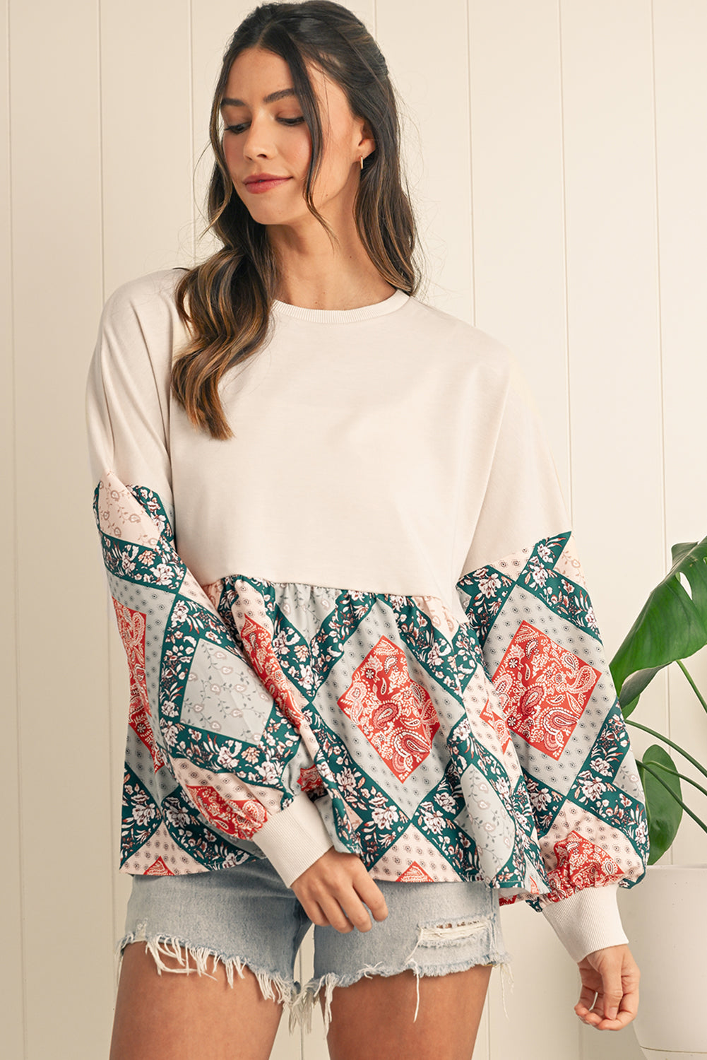 Woman wearing a white long-sleeve top with floral sleeves against a neutral background