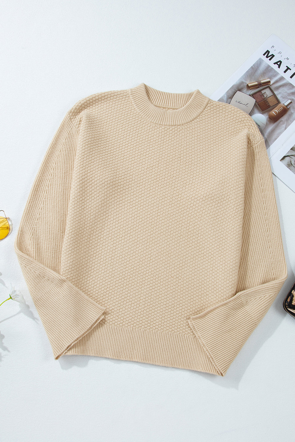 Beige sweater on a white surface with a magazine in the background