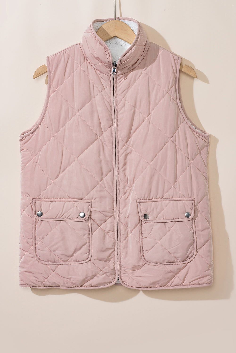 Pink quilted vest on a hanger against a beige background