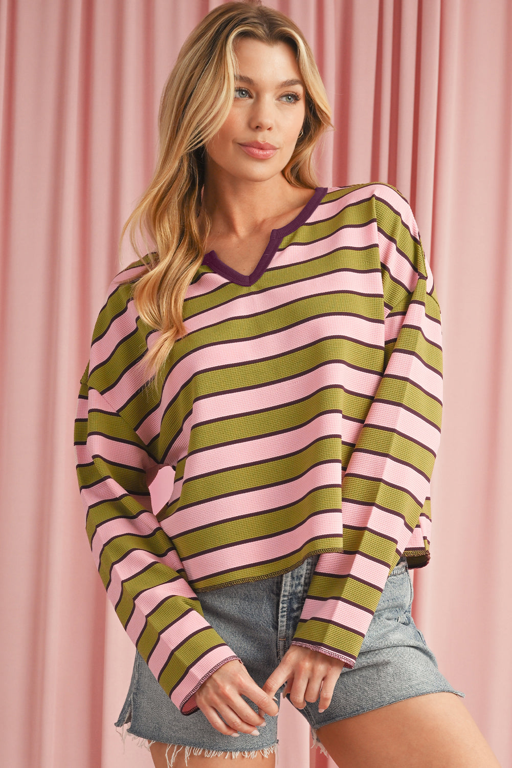 Woman wearing a pink and green striped sweater against a pink curtain background