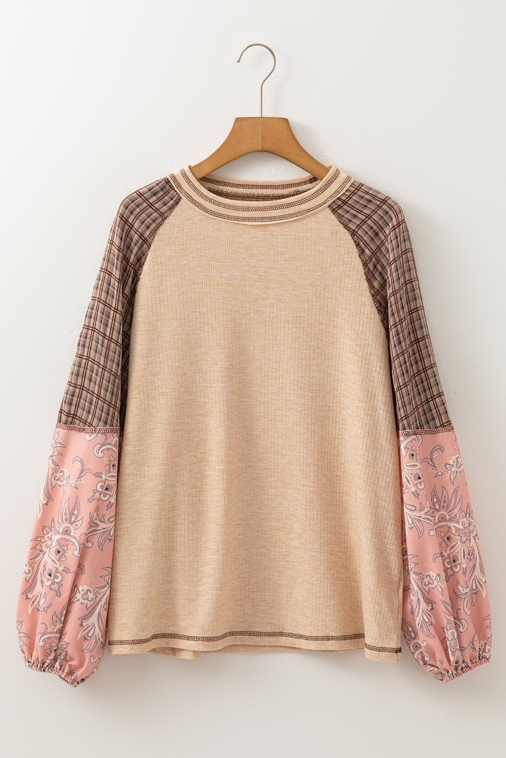 Beige sweater with plaid and floral sleeves on a wooden hanger against a white background