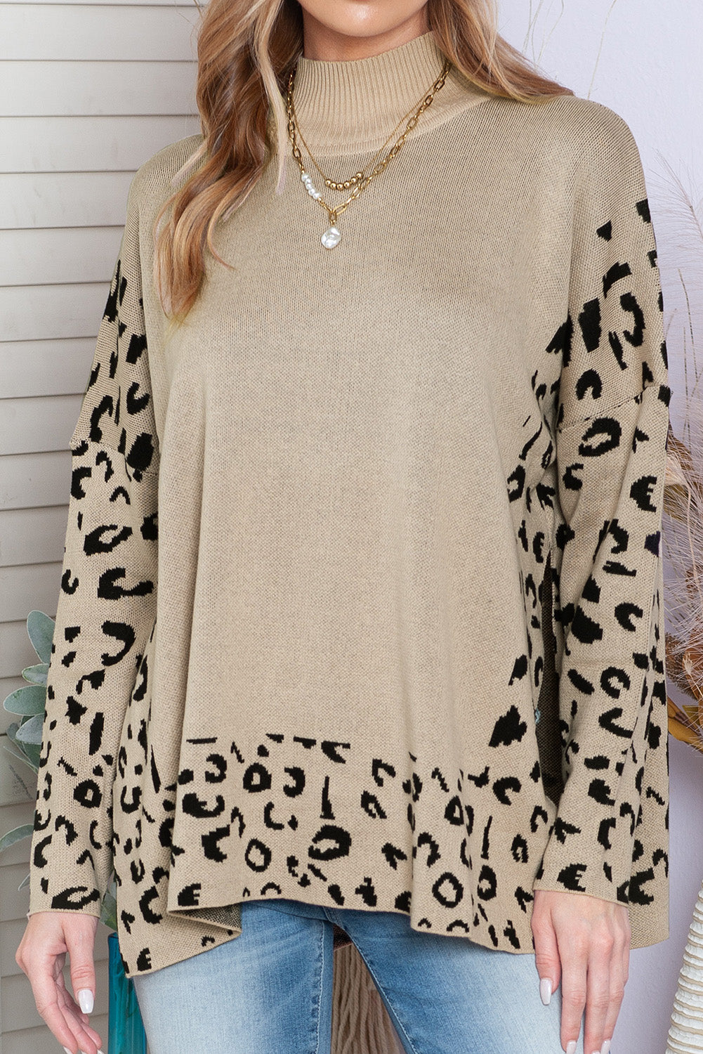 Beige sweater with leopard print sleeves worn by a person against a white wall.
