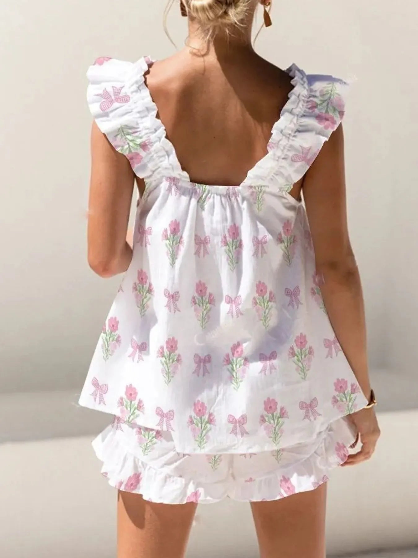 Woman wearing a white floral dress with ruffled sleeves and hem on a plain background