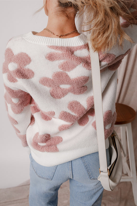 Person wearing a white sweater with pink floral patterns and blue jeans indoors.