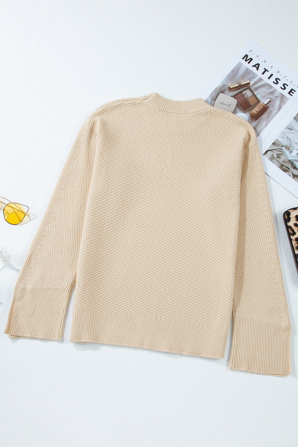 Beige sweater on a white background with a magazine underneath