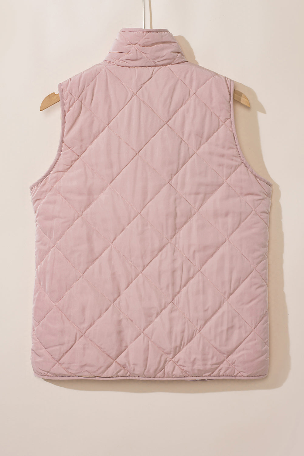 Pink quilted vest on a hanger against a beige background
