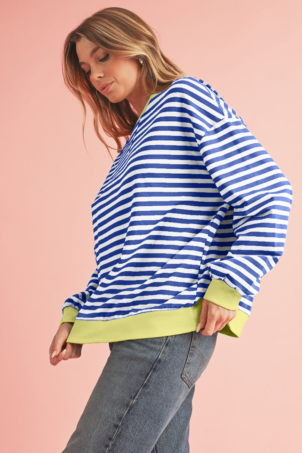 Woman wearing a blue and white striped sweater with green trim on a pink background