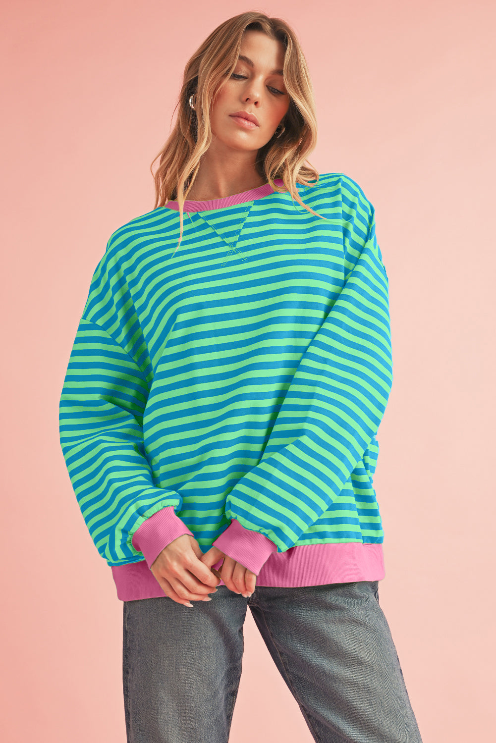 Woman wearing a green and pink striped sweater with pink cuffs and hem on a pink background