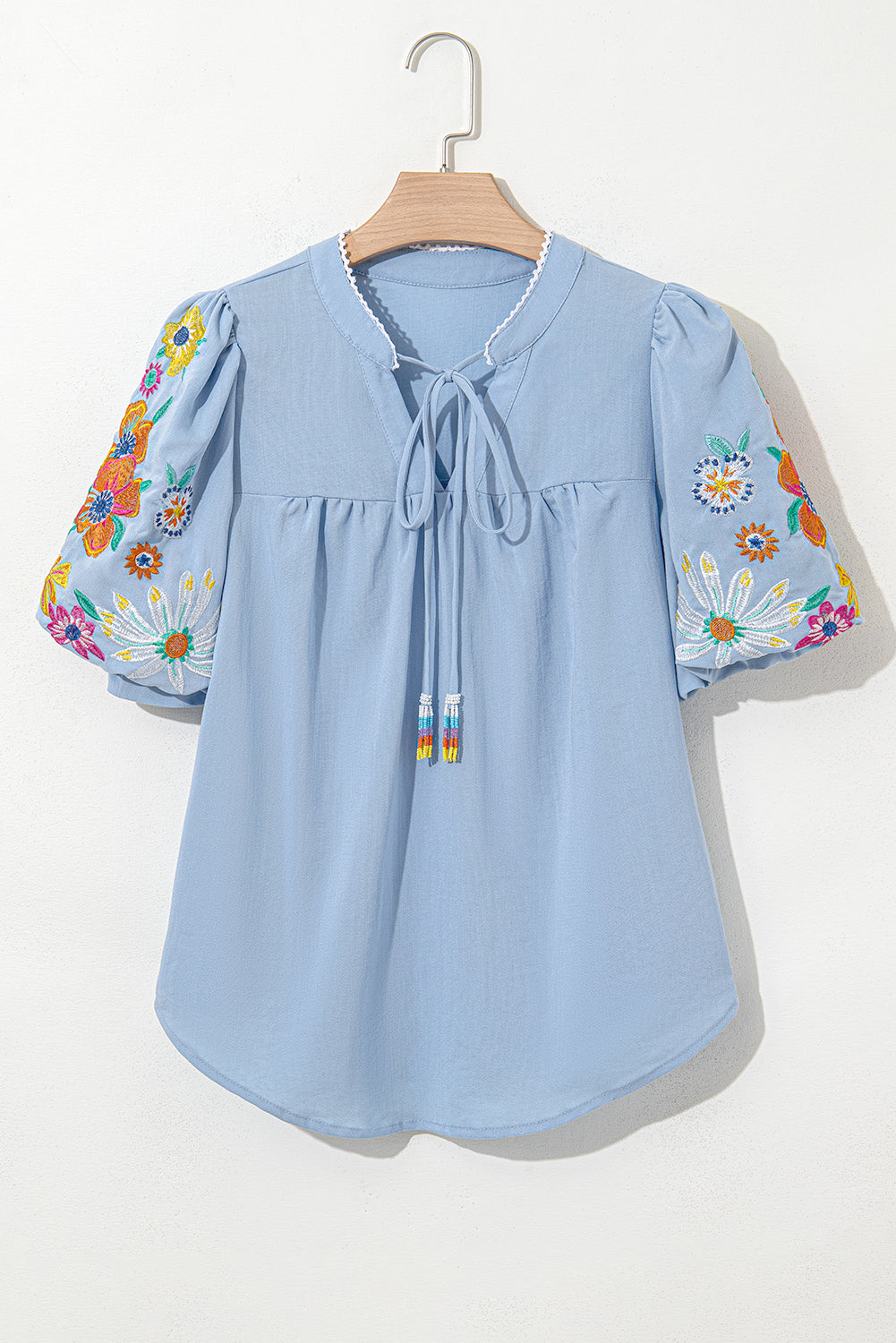 Light blue blouse with floral sleeves on a hanger against a white background