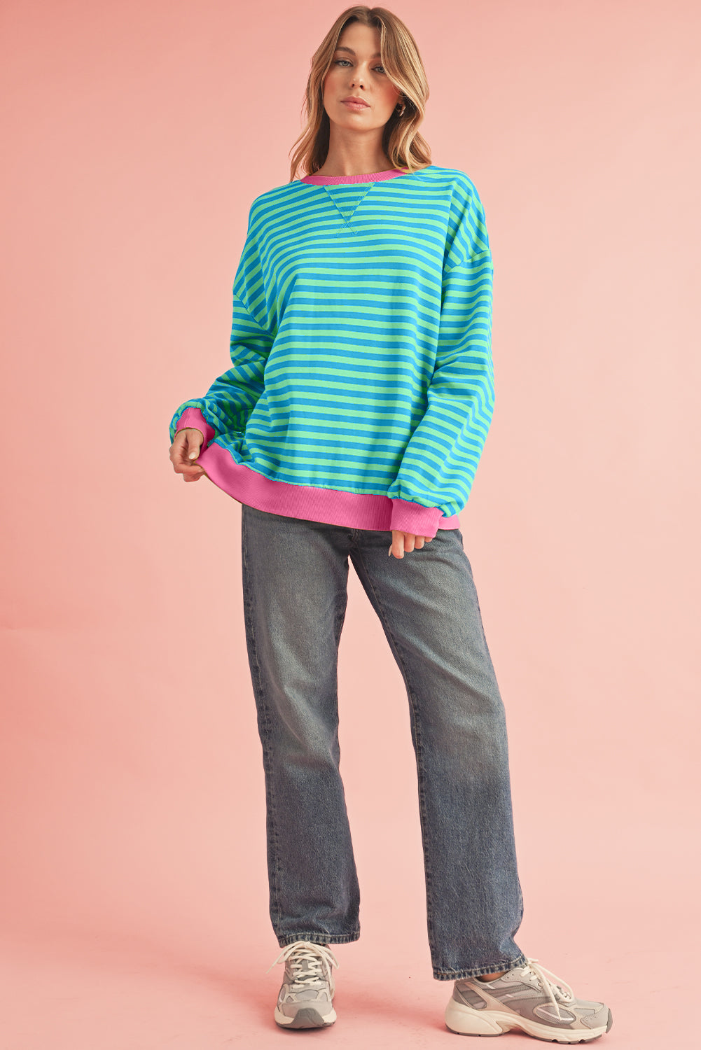 Woman wearing a blue and pink striped sweater with gray jeans on a pink background